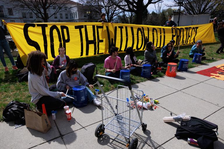 Menschen sitzen vor einem Banner mit der Aufschrift "Stoppen Sie das Willow-Ölprojekt". Menschen sitzen vor einem Banner mit der Aufschrift "Stoppen Sie das Willow-Ölprojekt".